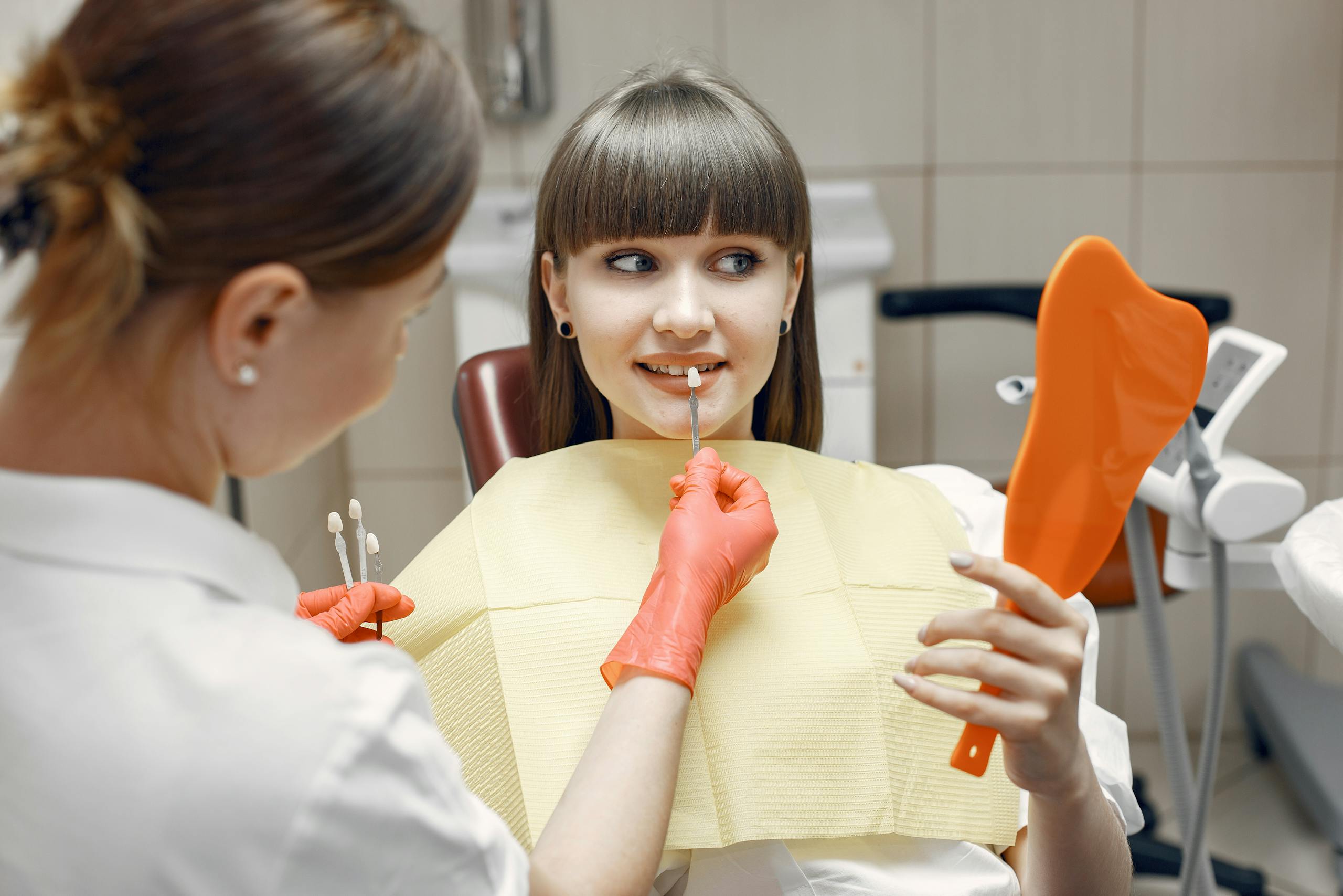 Porcelain Veneers 5 Dentist consults a young woman on veneers using dental tools and mirror in a clinic.