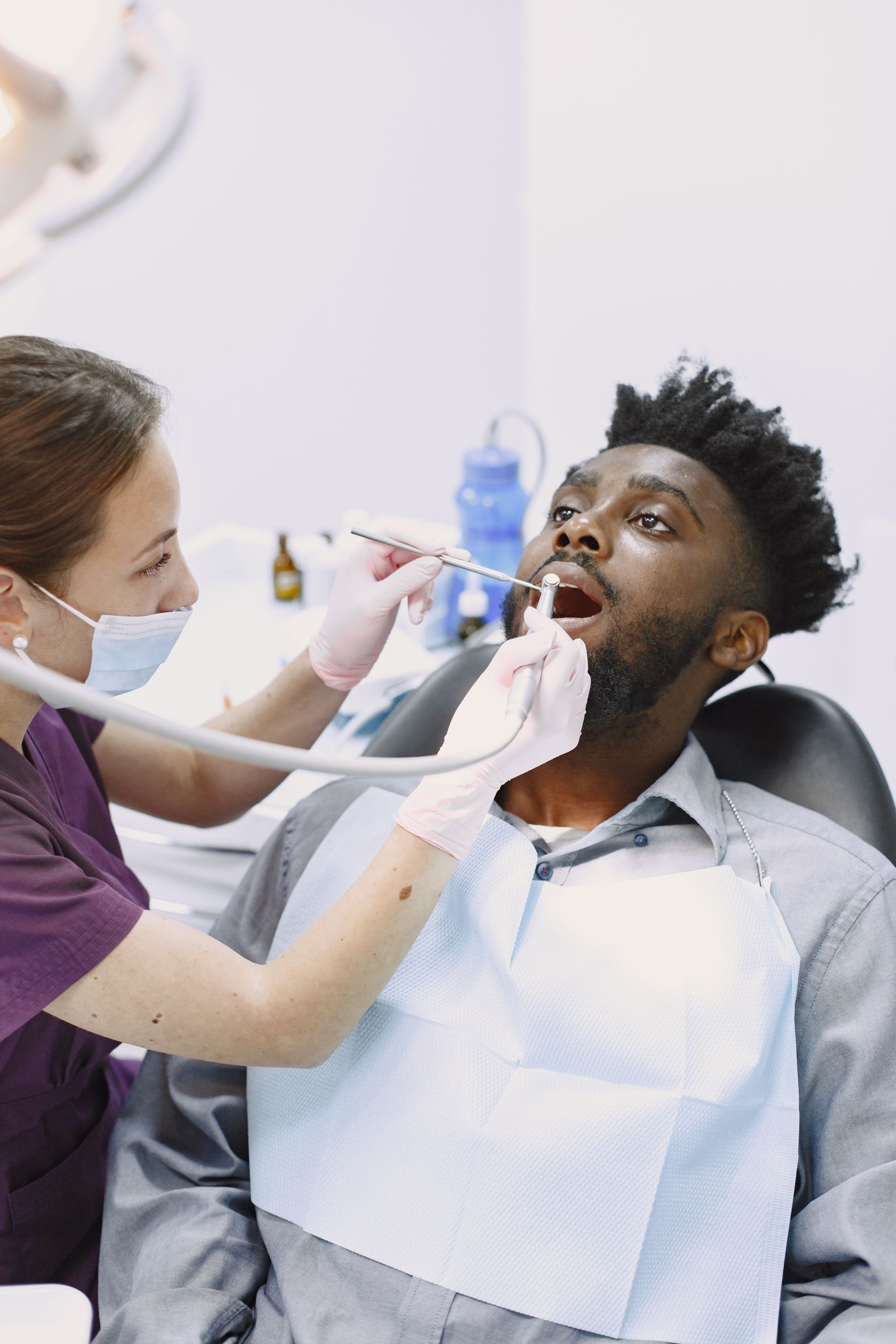 Black man undergoing routine dental checkup by a female dentist in a clinic.