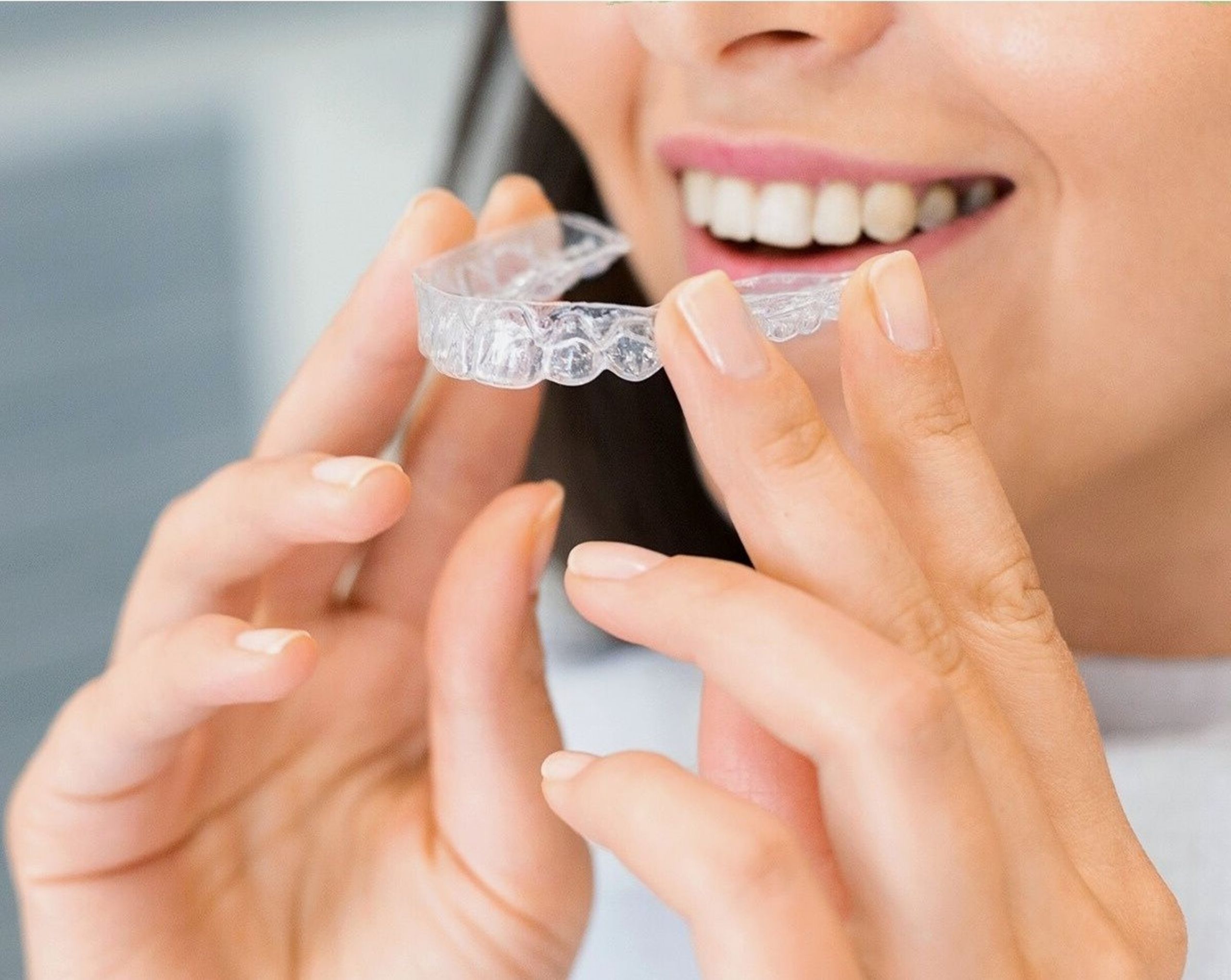 Invisalign 1 Close-up of a woman holding a clear dental aligner, showcasing dental health and a bright smile.