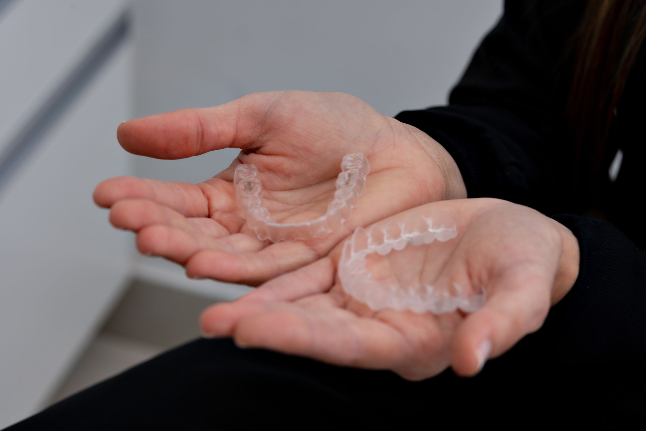 Invisalign 4 Close-up of hands holding clear dental aligners in a dental clinic setting.