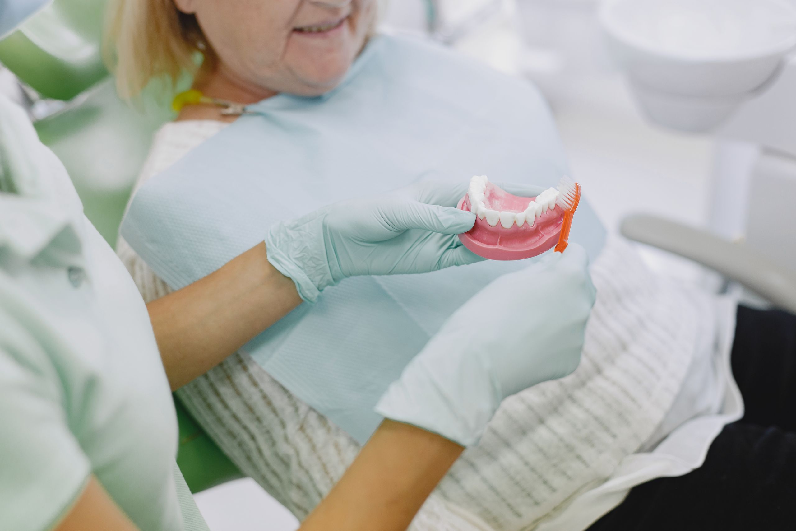 Partial and Complete Dentures 1 Senior woman in dental chair being shown denture brushing technique by a dental professional.